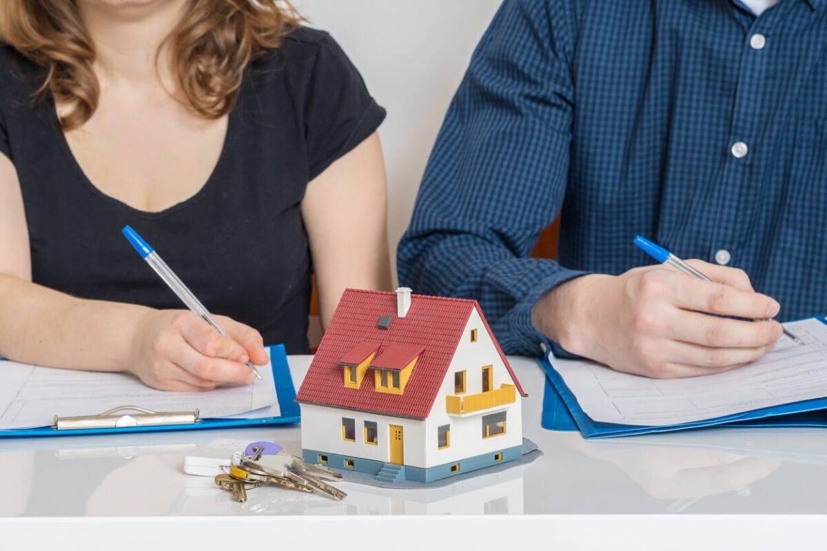 Spring Cleaning Your Marriage: What Happens To Your Home?- two people signing paperwork with a little house in the middle